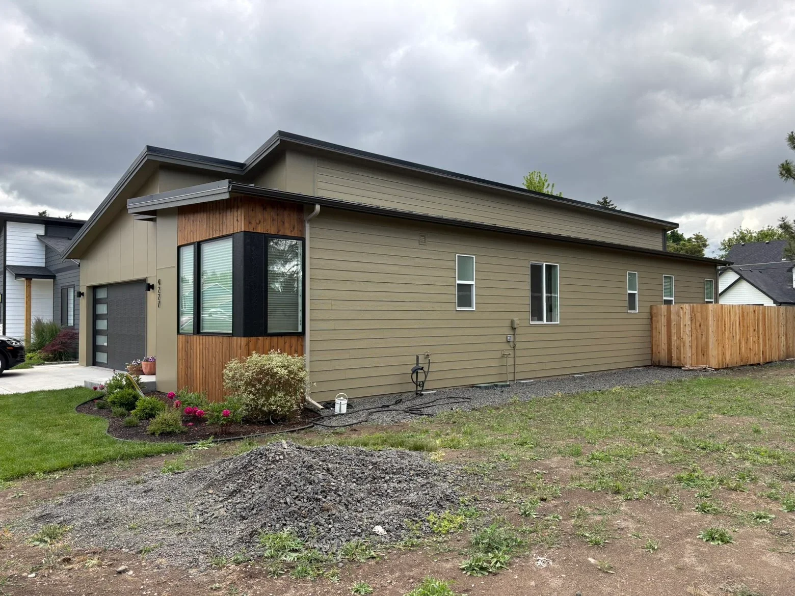 Tan fiber cement siding with cedar accents, black-framed windows, dark roof, and gravel landscaping