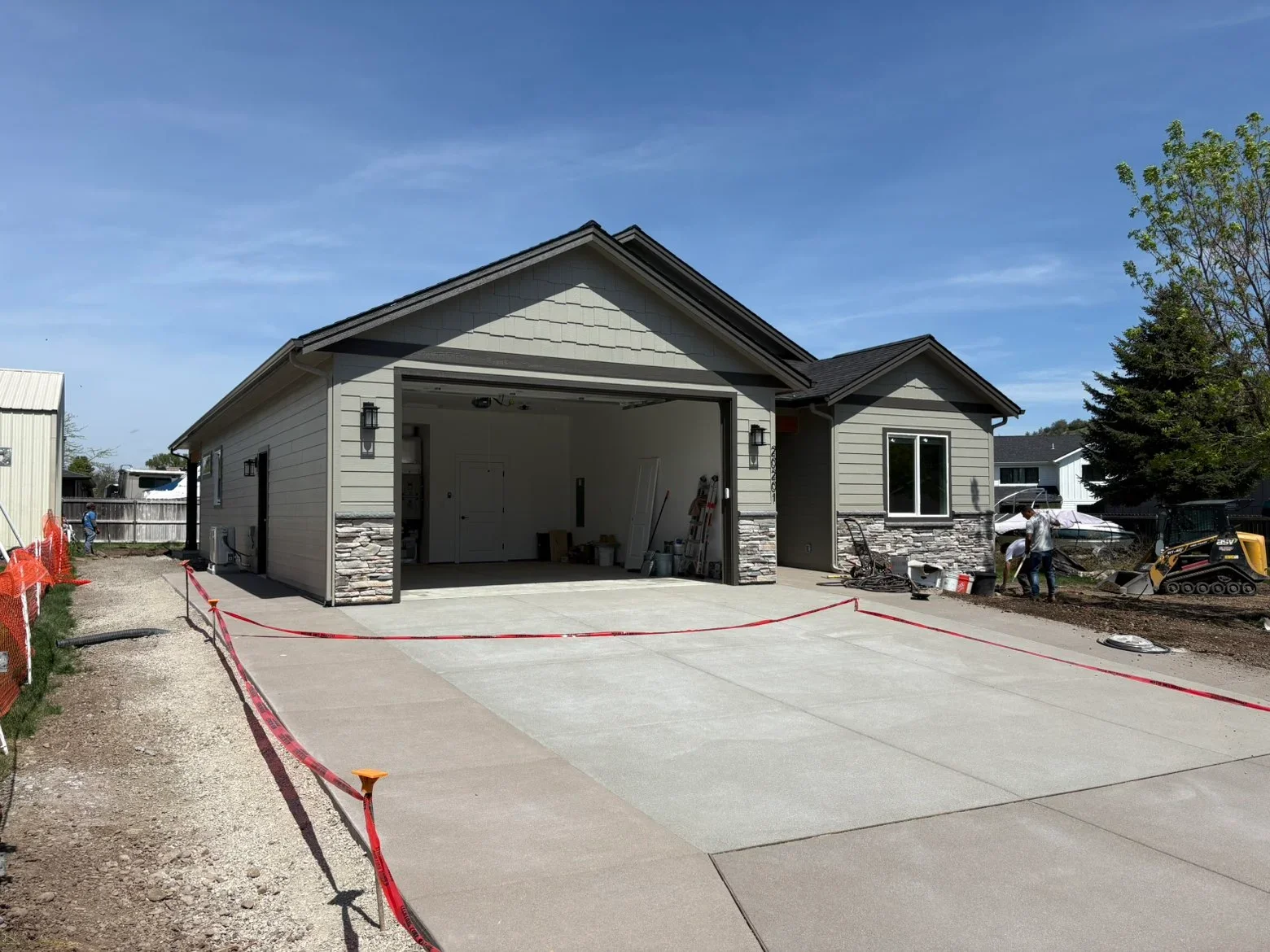New garage with gray fiber cement siding, stone veneer base, dark roof, and concrete driveway