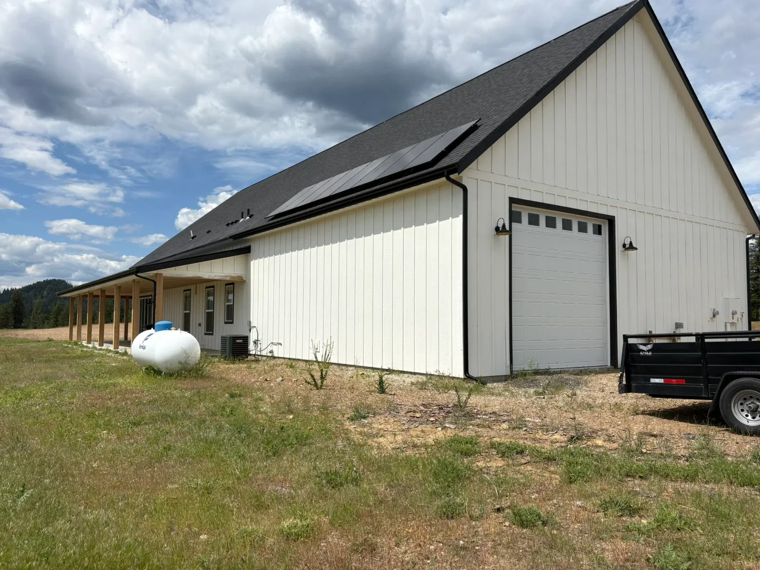 Dark gray metal standing seam roof on white vertical siding agricultural building with gable design