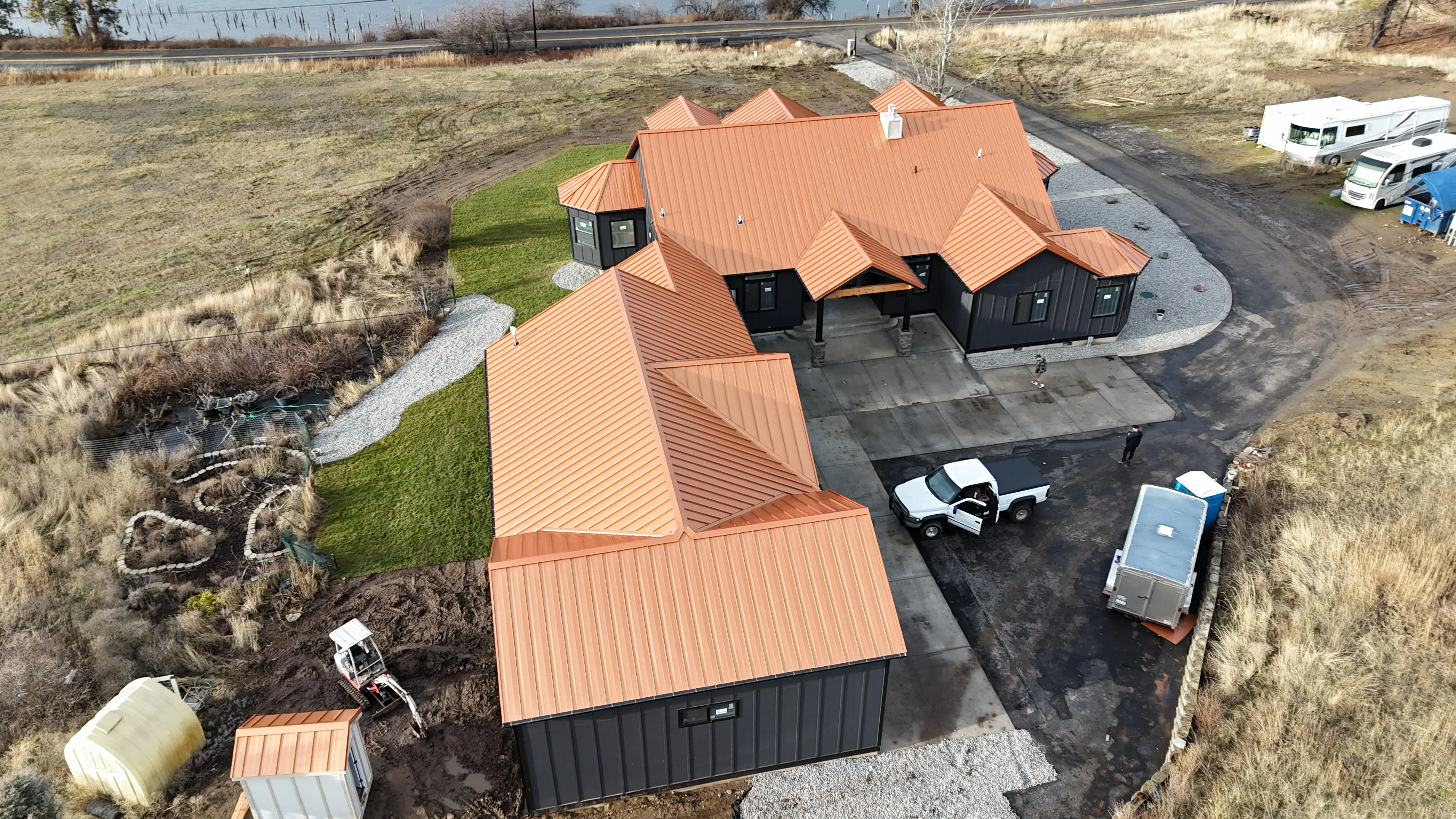 Copper-colored metal standing seam roof with multiple peaks on black metal-sided residential building