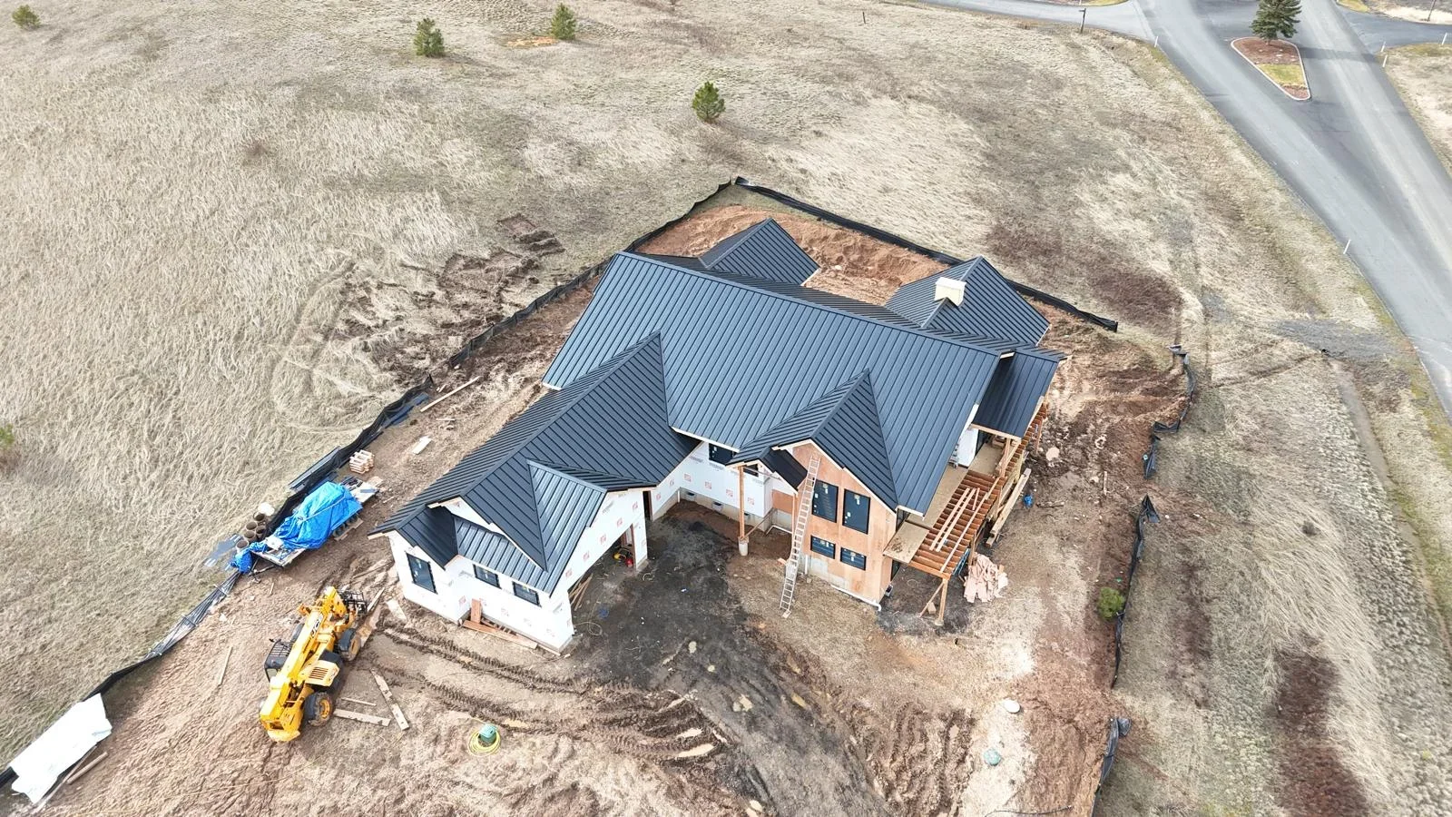 Dark gray standing seam metal roof on multi-gable residential home during construction