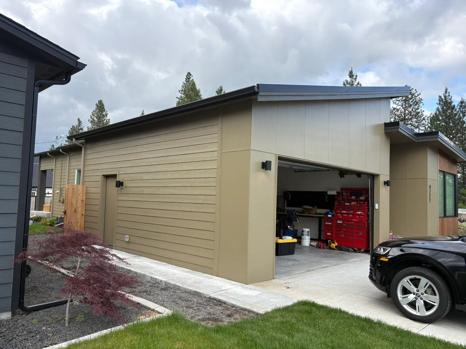 Modern garage with standing seam metal roof, tan horizontal siding, black trim, and concrete driveway