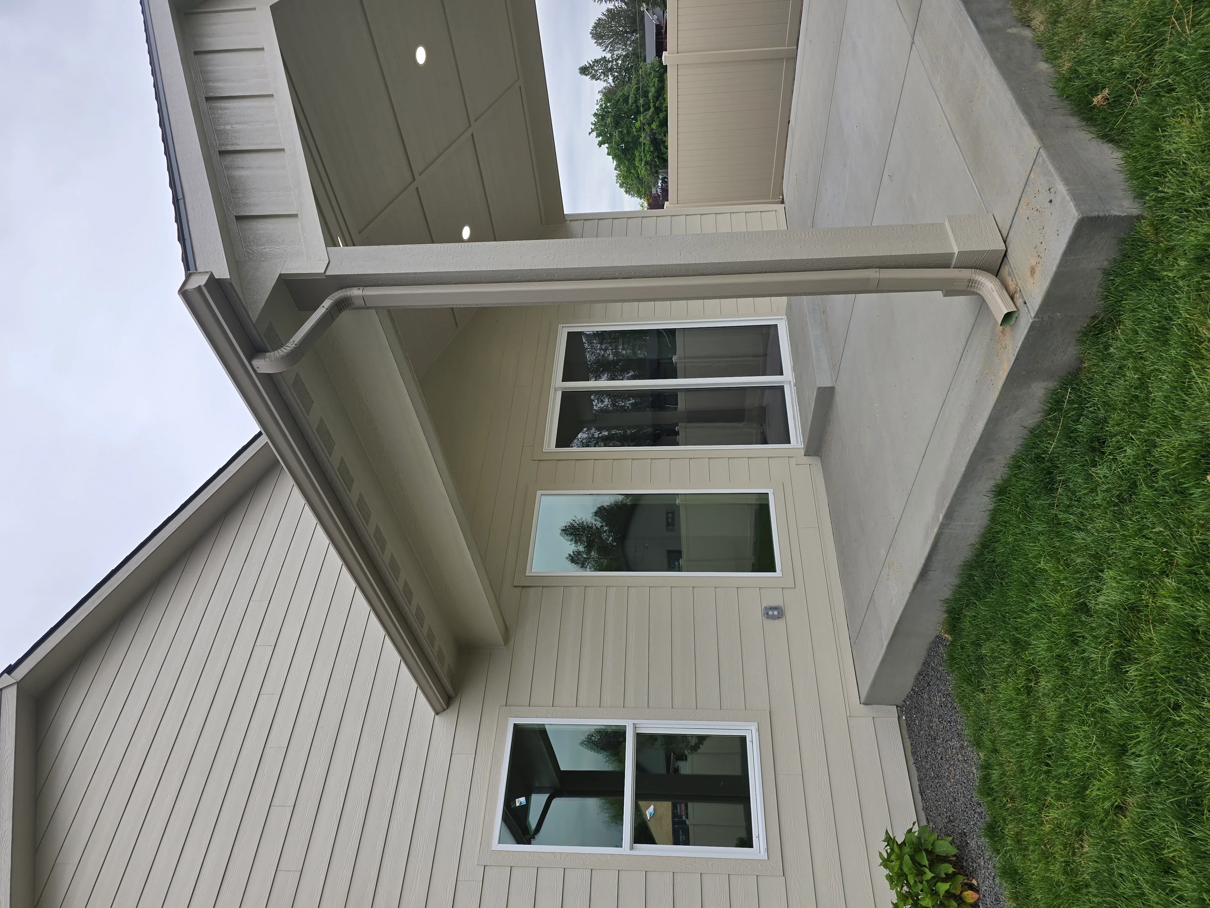 Light gray vertical siding with new soffit, fascia, gutters, and window trim on residential home