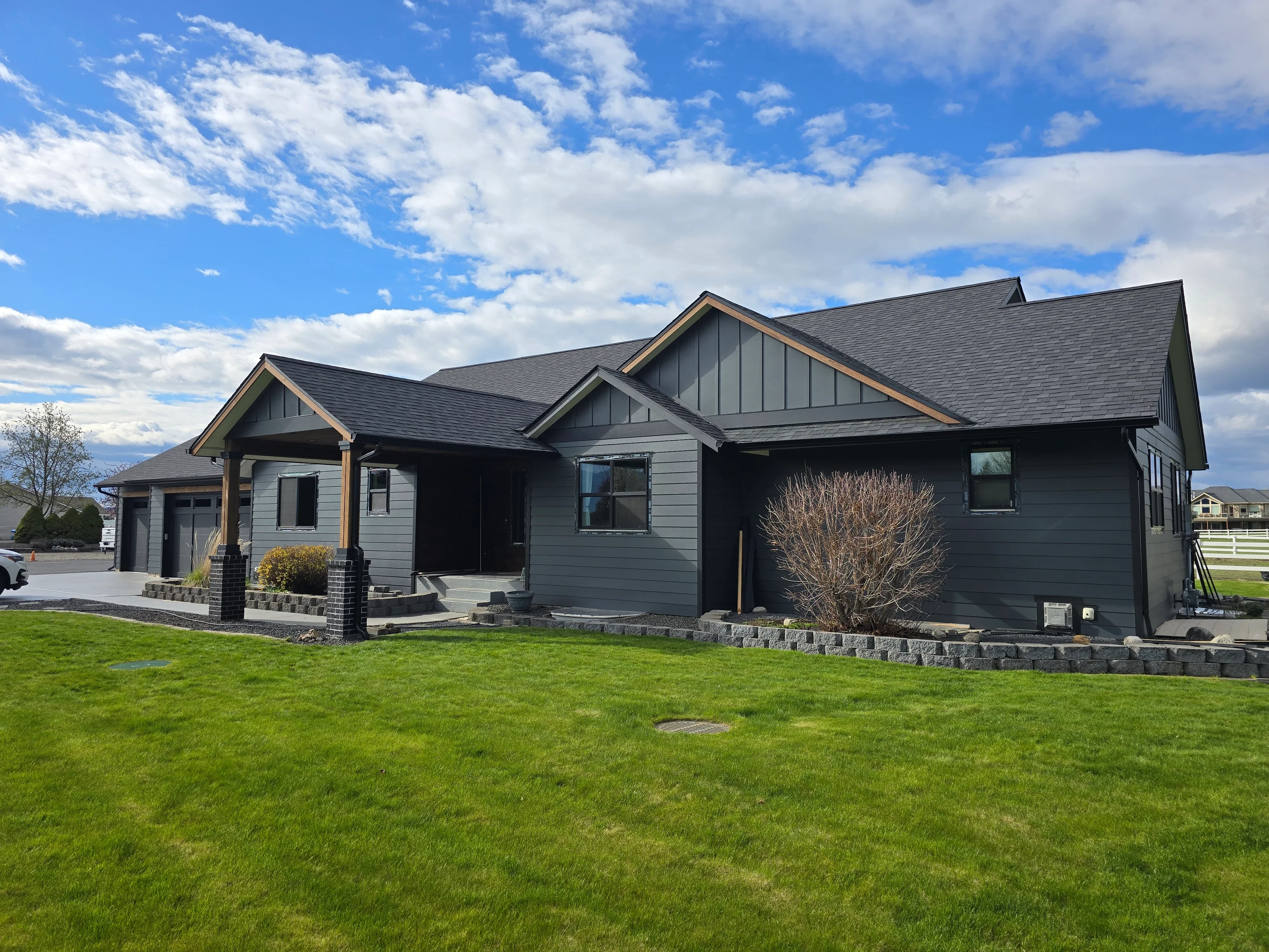 Charcoal gray architectural shingles, stone foundation veneer, fiber cement siding, multi-plane roof installation