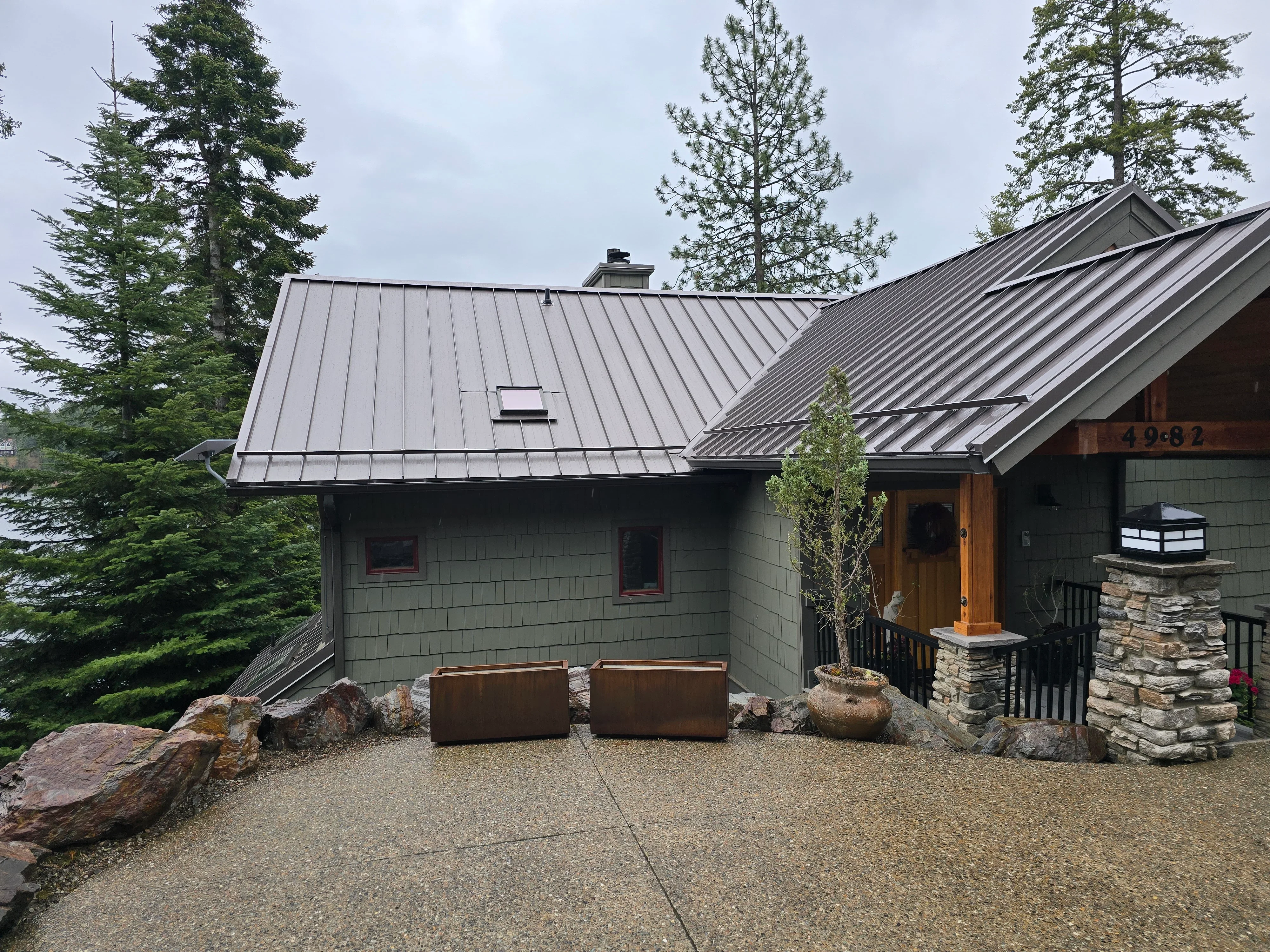 Standing seam metal roof with gray finish on modern home with stone chimney and wood siding