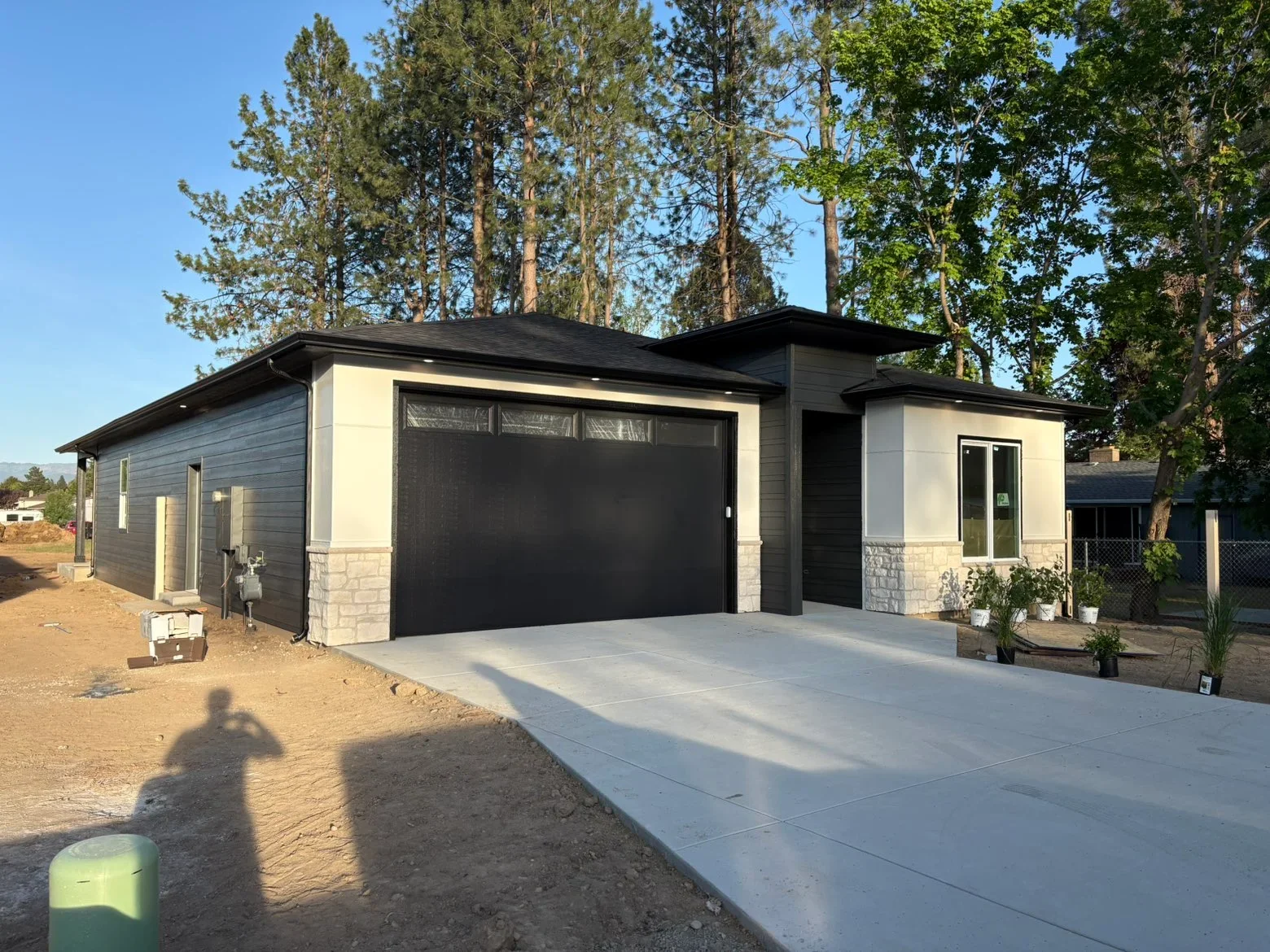 Modern garage with black metal roof, dark siding, cream panels, and stone veneer base