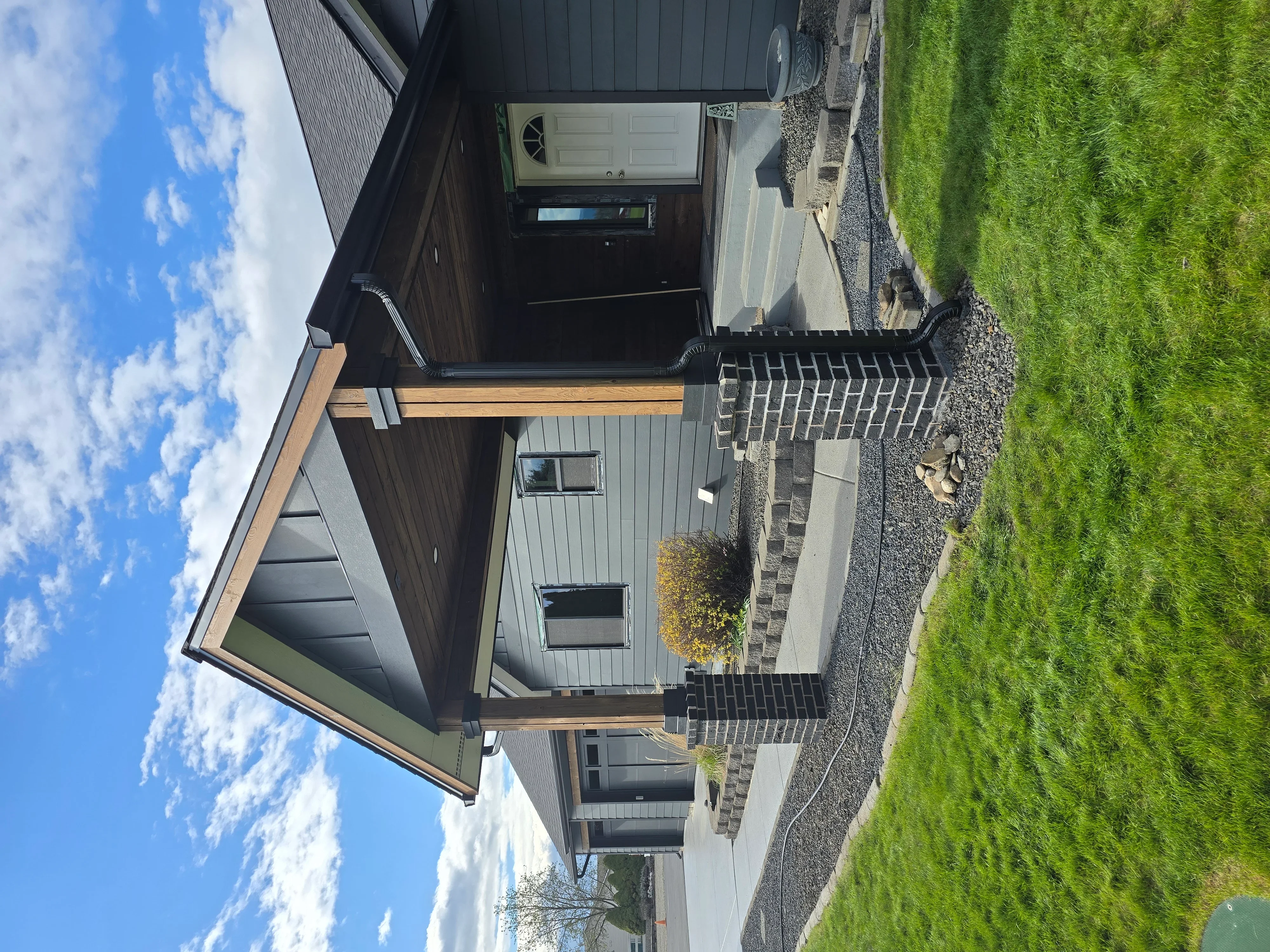 Metal standing seam roof, dark siding, stone chimney, and brick paver entry on modern home