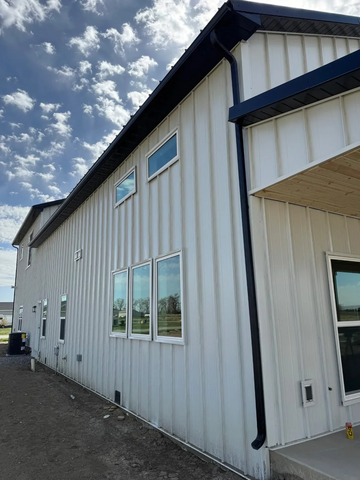 White corrugated metal siding with dark trim, aluminum windows, and installed gutters on agricultural building