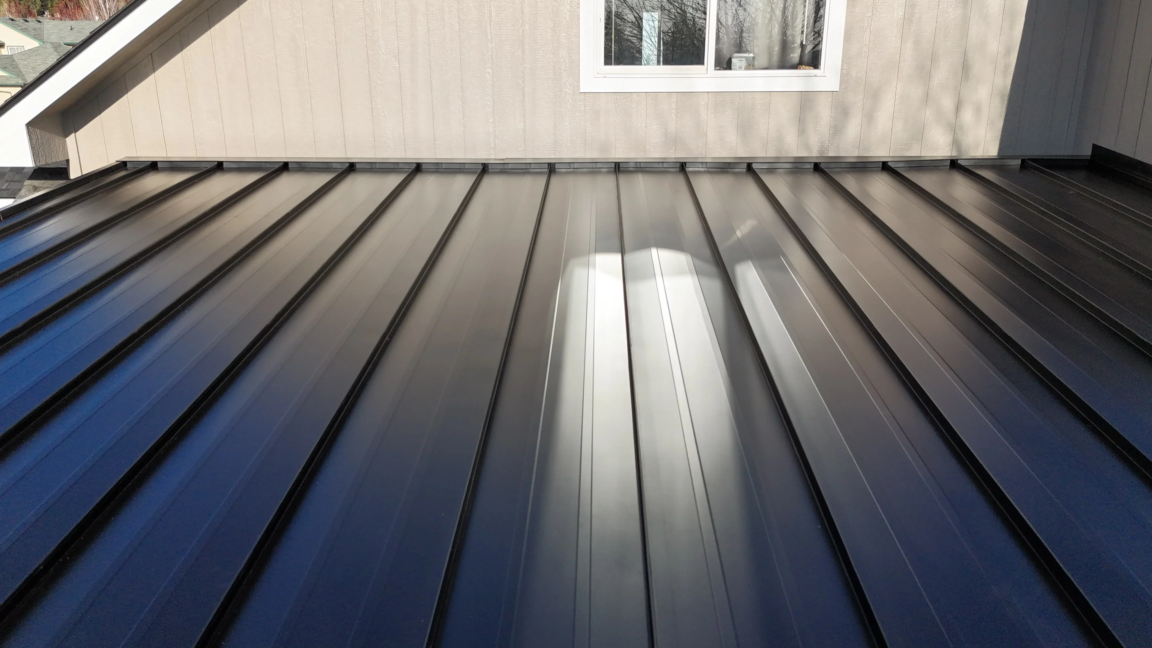 Standing seam metal roof with vertical ribs, dark blue to silver gradient panels, clean seams