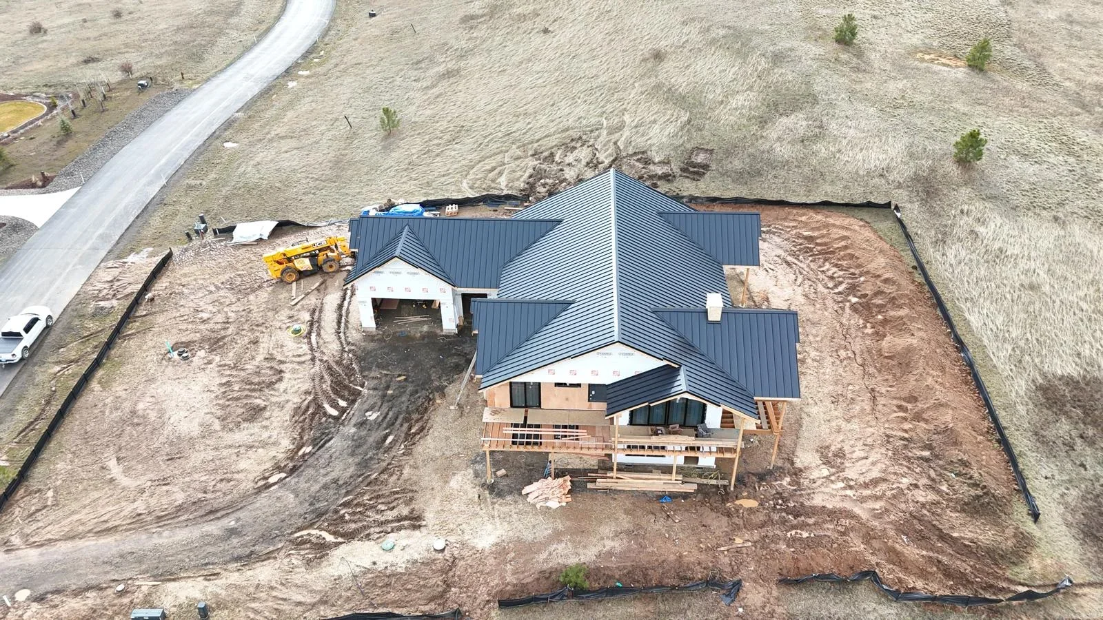 Standing seam metal roof installation on residential home with dark gray panels and complex multi-pitch design