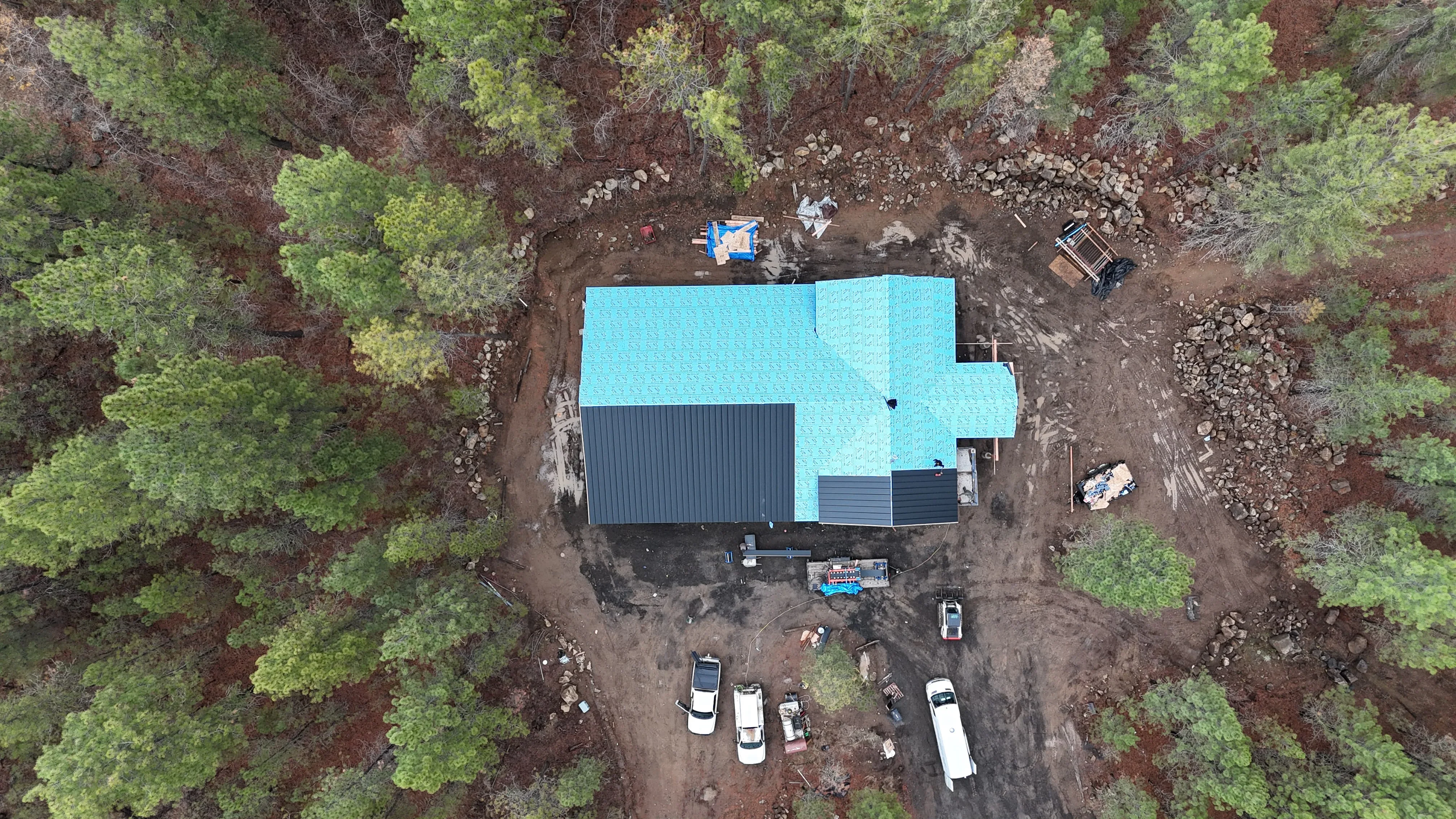 Aerial view of metal roof installation with turquoise standing seam panels and dark metal roofing sections