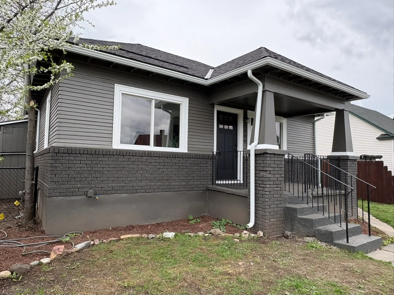Dark gray asphalt shingle roof, charcoal siding, brick foundation, and metal porch railings on residential home