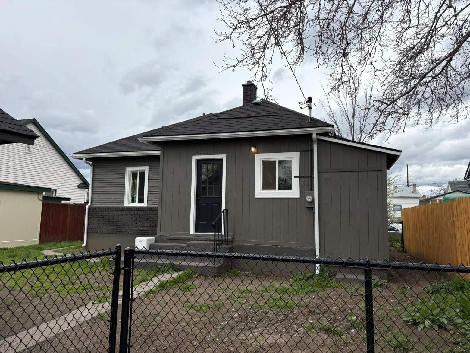 Dark gray asphalt shingle roof on bungalow with brick chimney and white-trimmed windows
