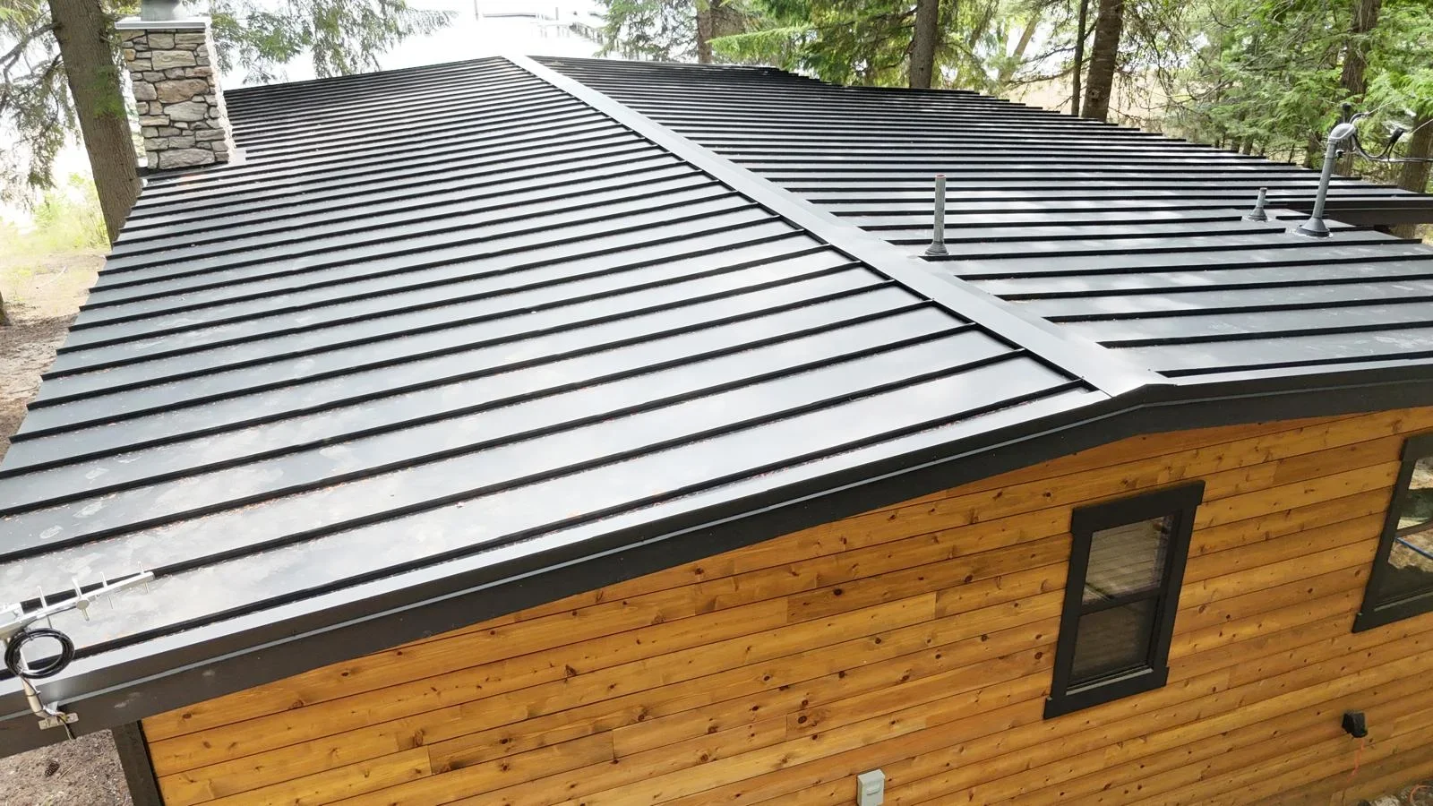 Standing seam metal roof with black panels and horizontal seams on log cabin structure