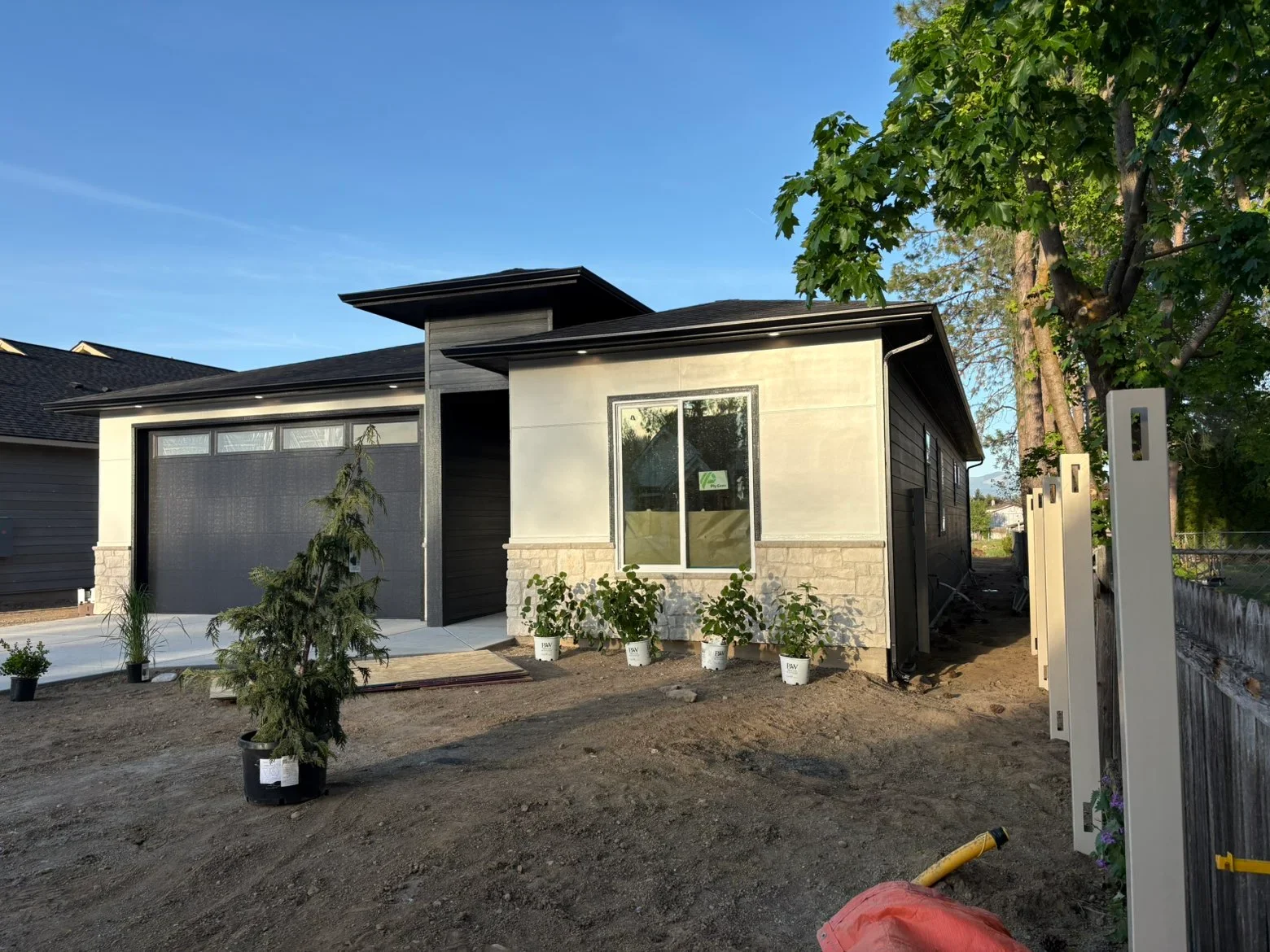 Modern home exterior with cream siding, black trim, stone veneer, and dark garage door under construction