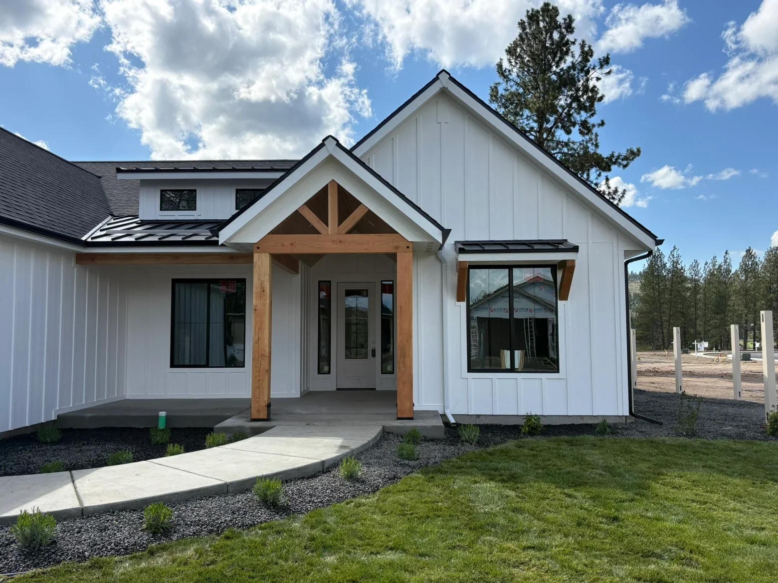 Standing seam metal roof with black trim on modern farmhouse with white siding and wood gable beams