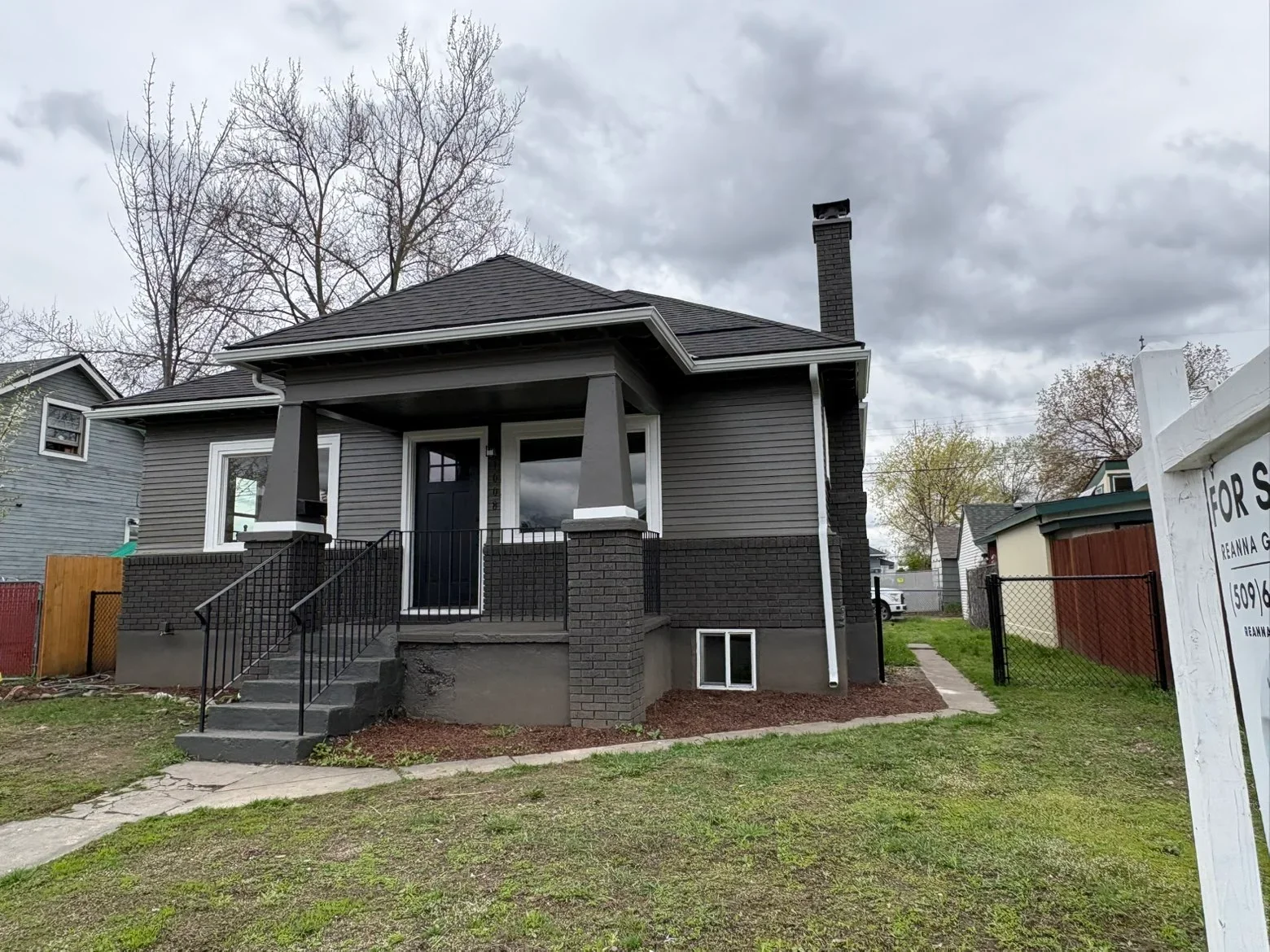 Dark gray architectural shingle roof, dark siding, white trim, brick chimney, covered porch with metal railings