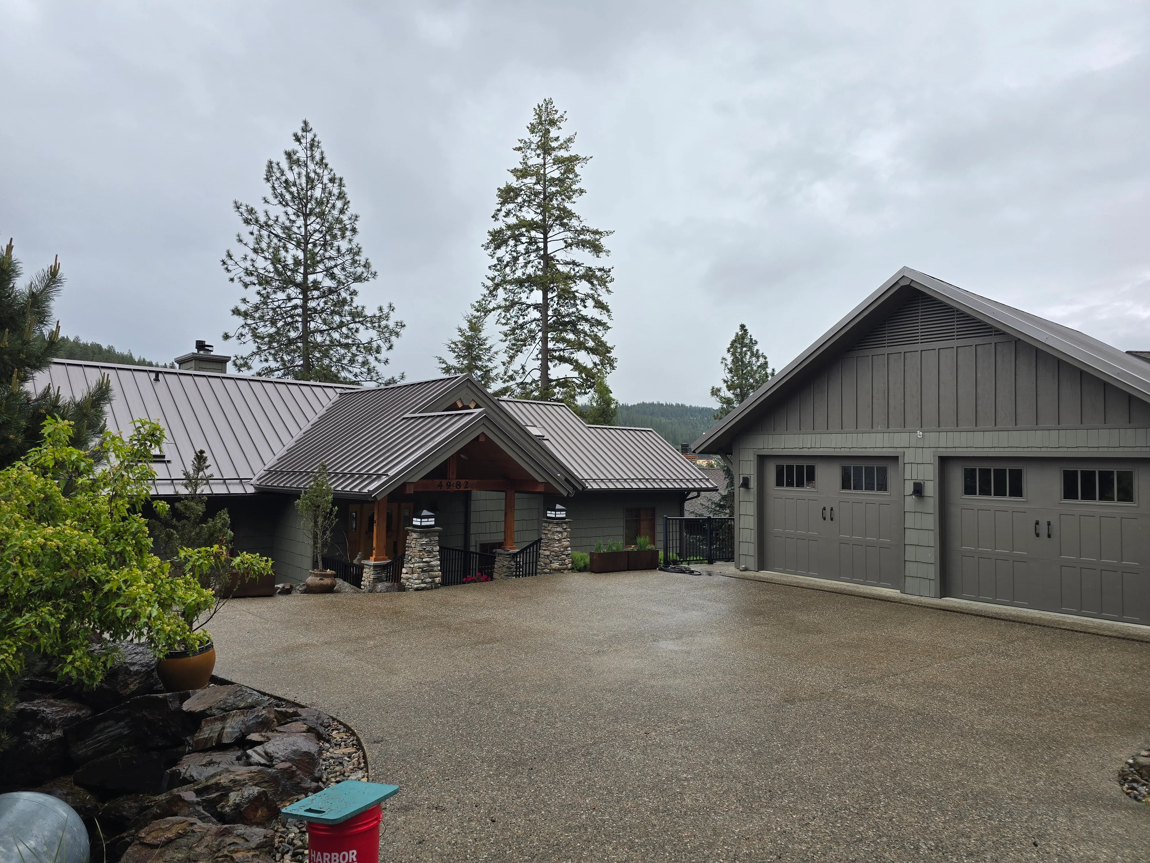 Dark gray standing seam metal roof on modern home with stone veneer and board-and-batten siding