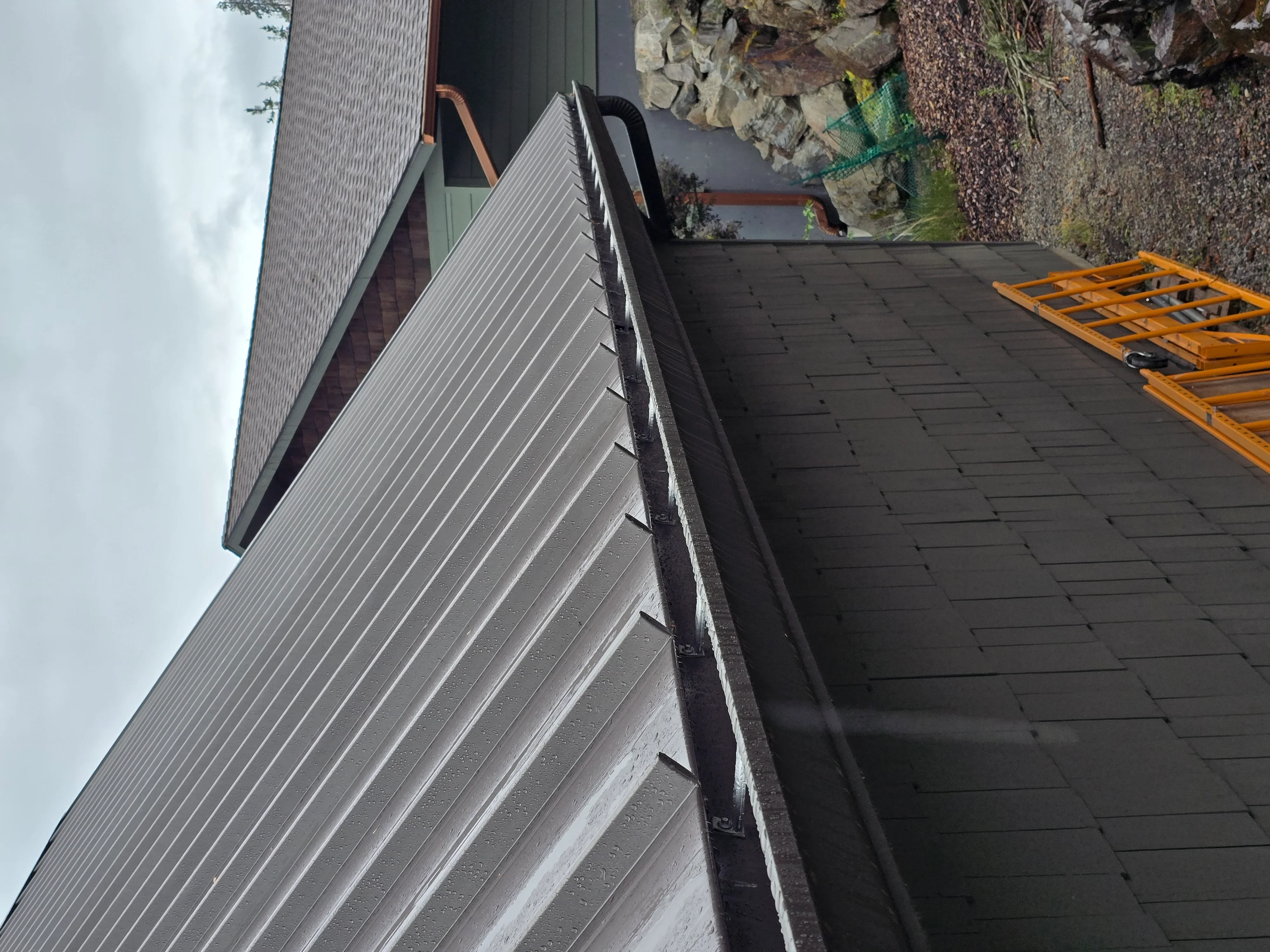 Gray standing seam metal roof with vertical ribs, copper downspouts, and integrated gutter system
