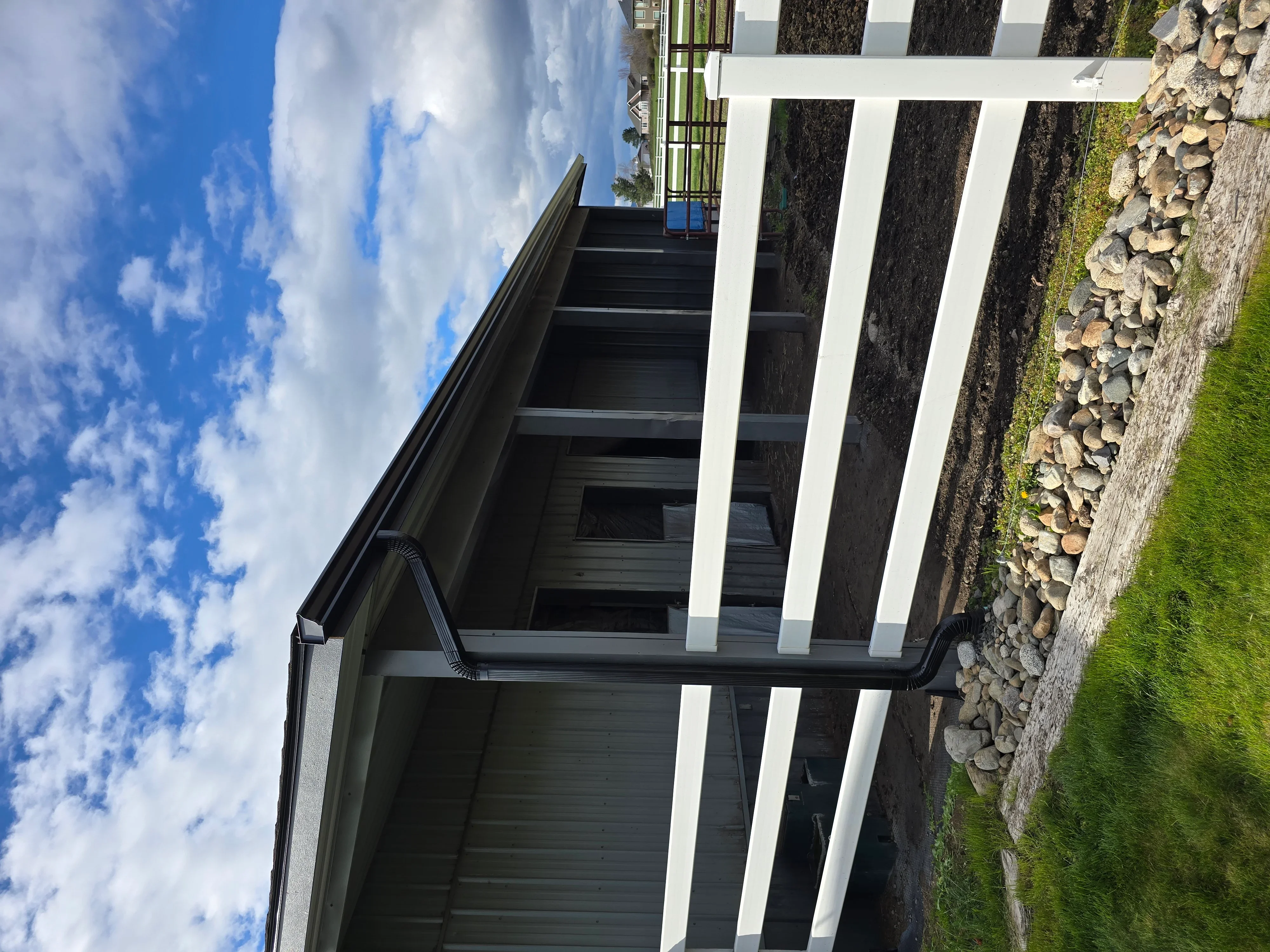 White vertical siding panels with dark wood cladding, modern gutter system, river rock landscaping