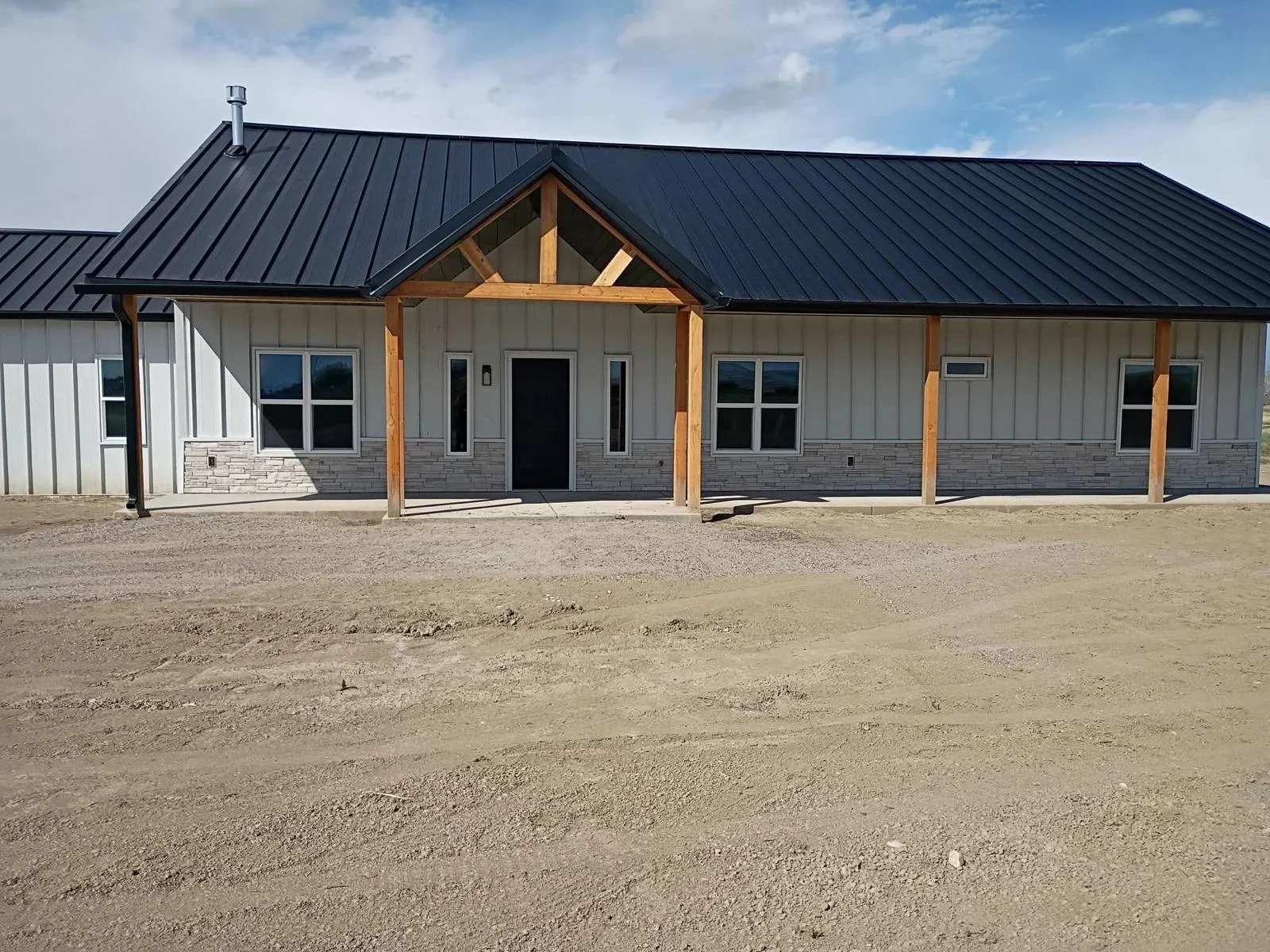 Black standing seam metal roof on modern residential building with timber accents and stone veneer