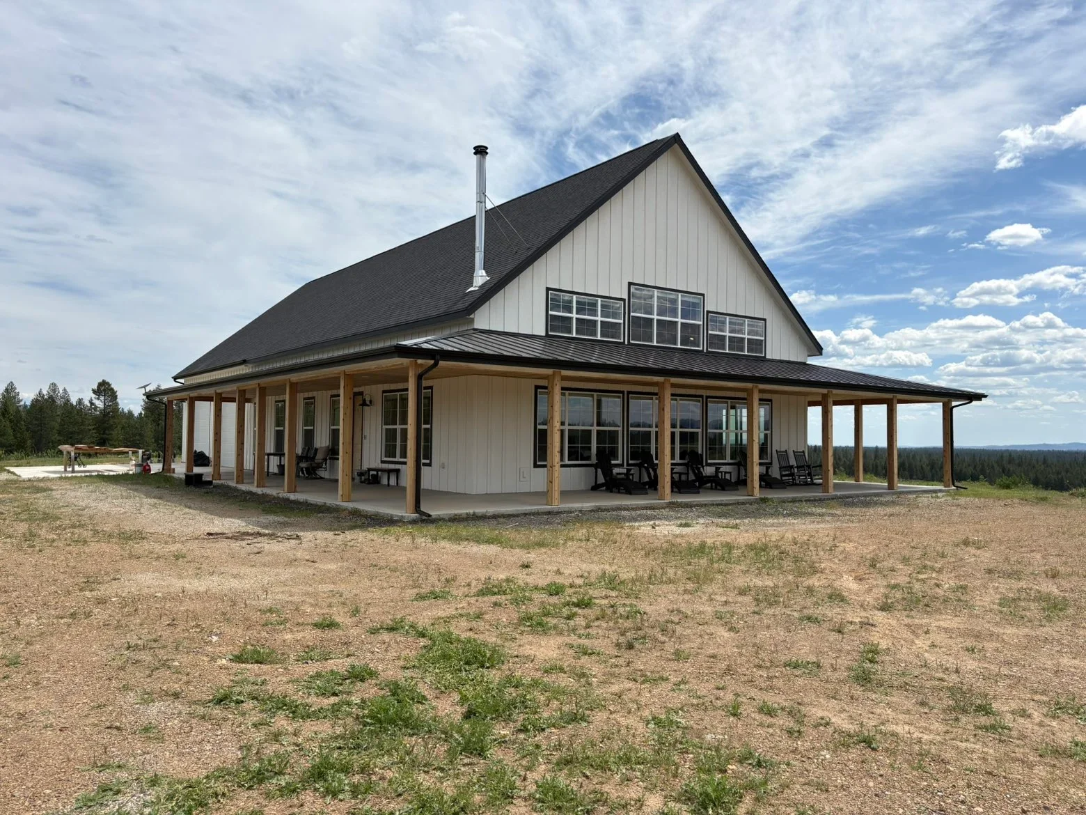 Standing seam metal roof with dark shingles, white siding, and wood beam porch on modern farmhouse