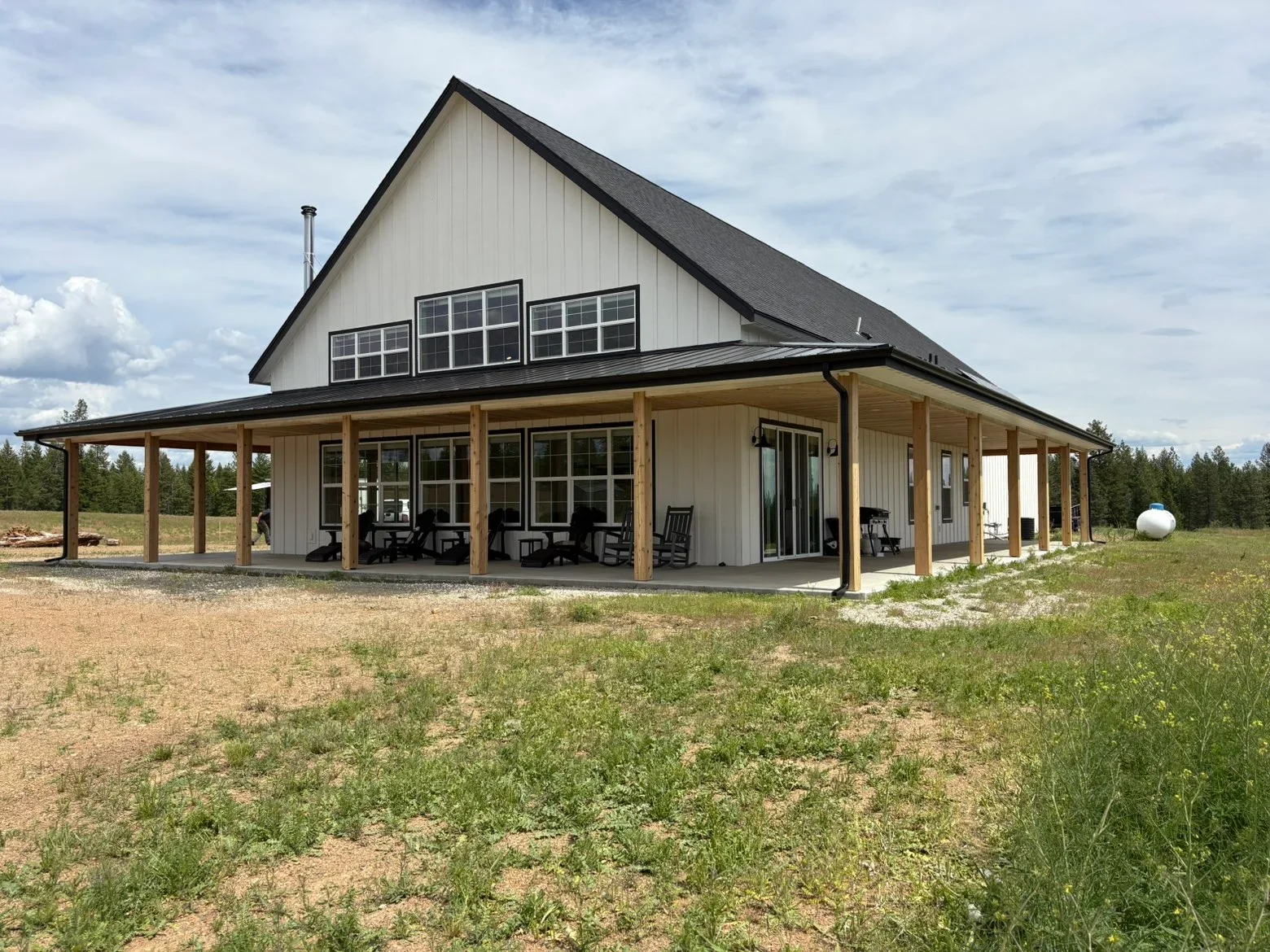 Steep gable roof with dark shingles, white vertical siding, and wooden porch columns on modern farmhouse