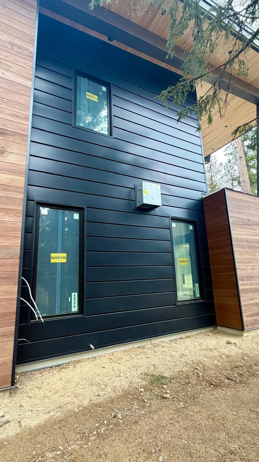 Black horizontal fiber cement siding with integrated windows and wood accent panels