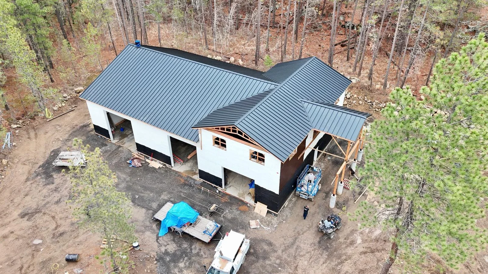 Standing seam metal roof installation in charcoal gray on residential home with white walls and timber accents