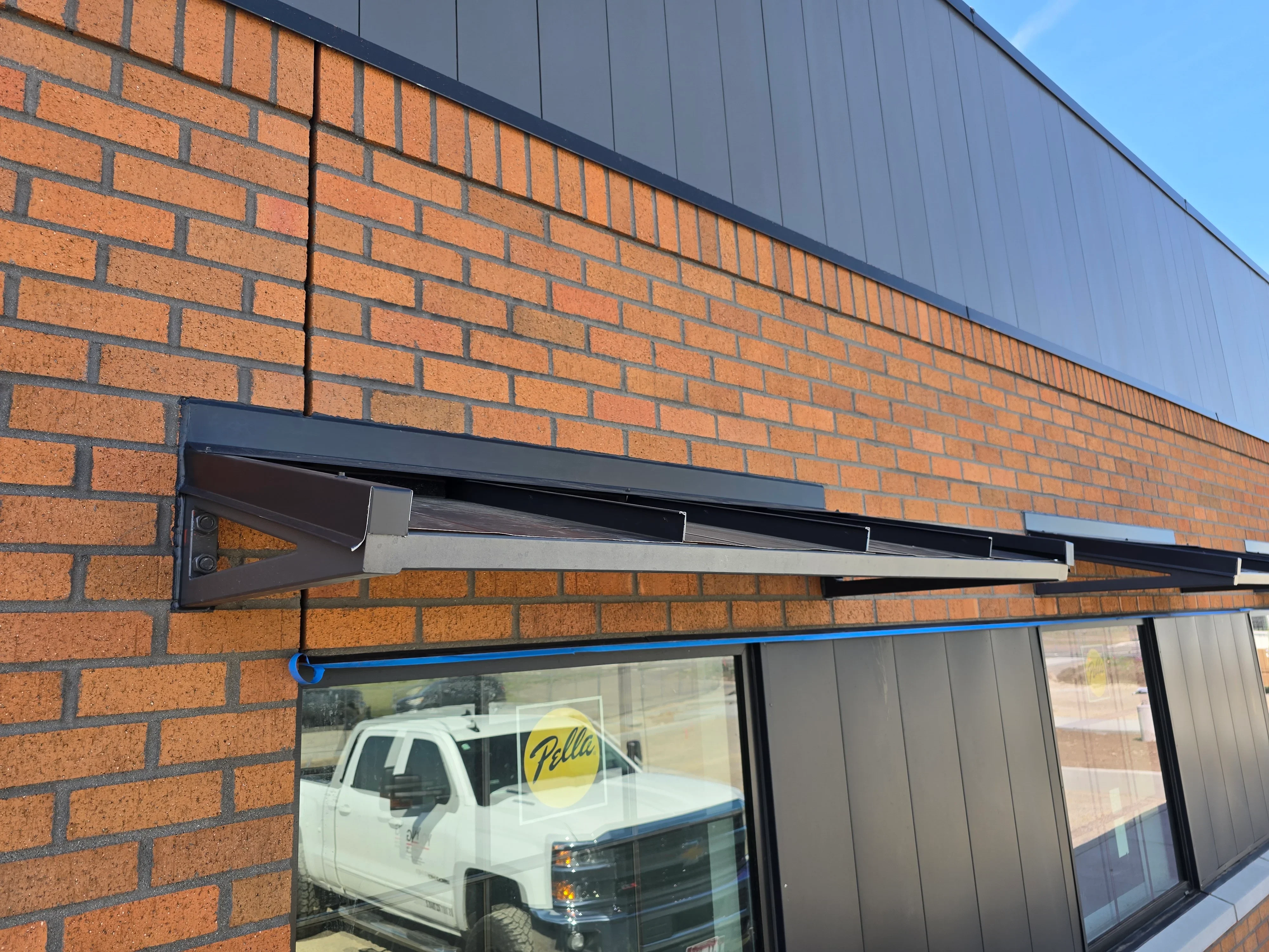 Dark metal awning with gutter system installed on brick commercial storefront