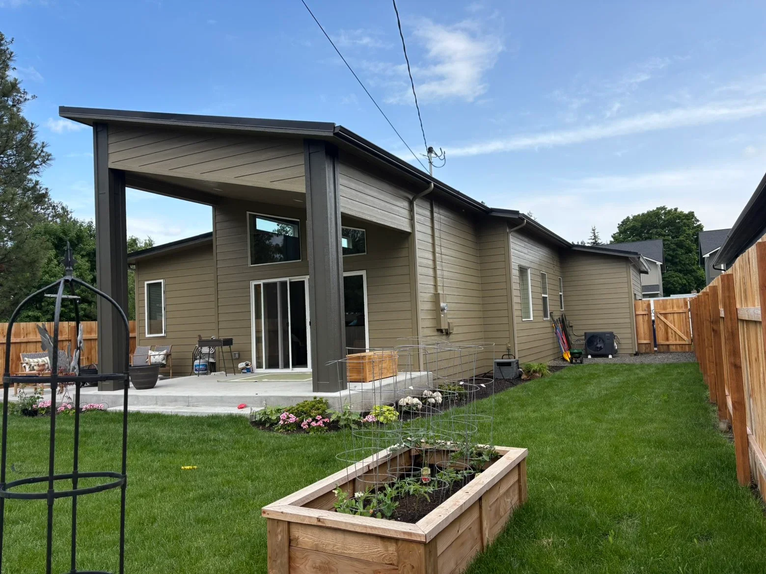 Modern home with tan fiber cement siding, dark-trimmed covered patio, flat roof overhang, and concrete patio